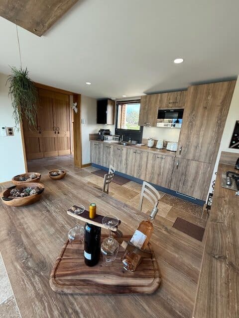Cuisine moderne en bois avec table à manger, bouteilles de vin et décoration rustique dans un intérieur élégant.