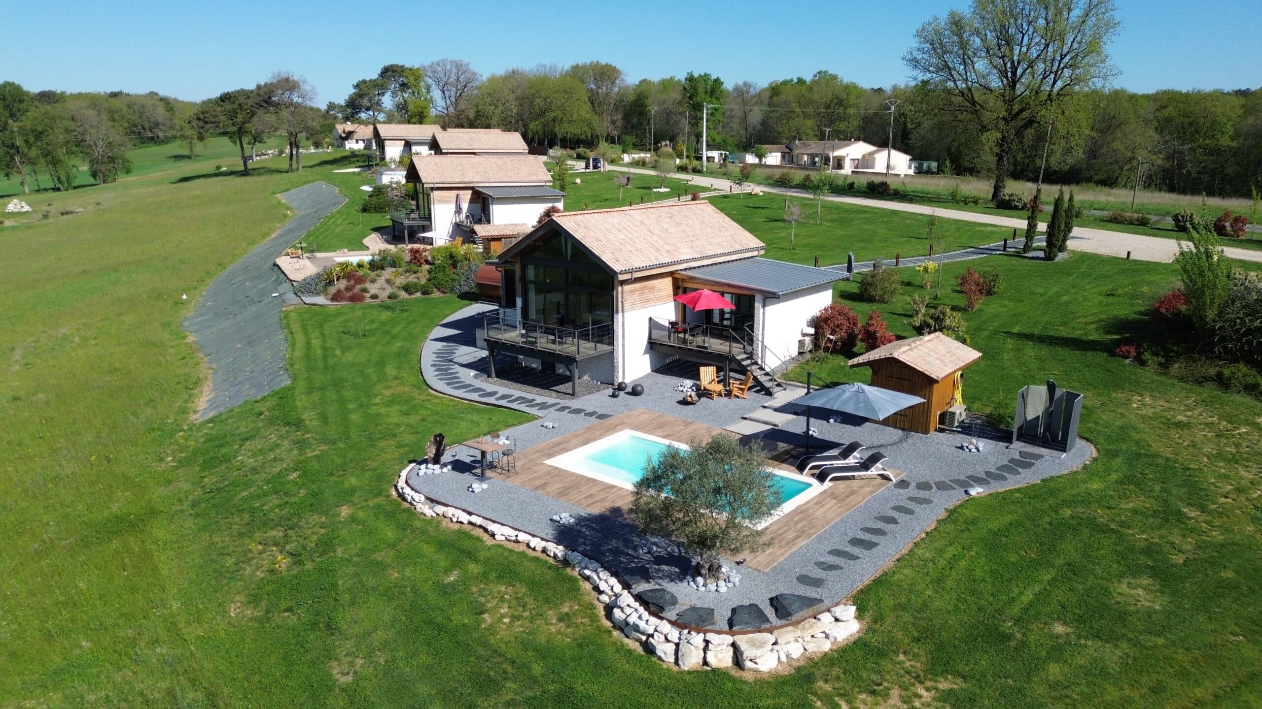 Villas modernes avec piscine, terrasses et jardins verdoyants. Architecture contemporaine sous ciel bleu, espace extérieur paisible et aménagé.